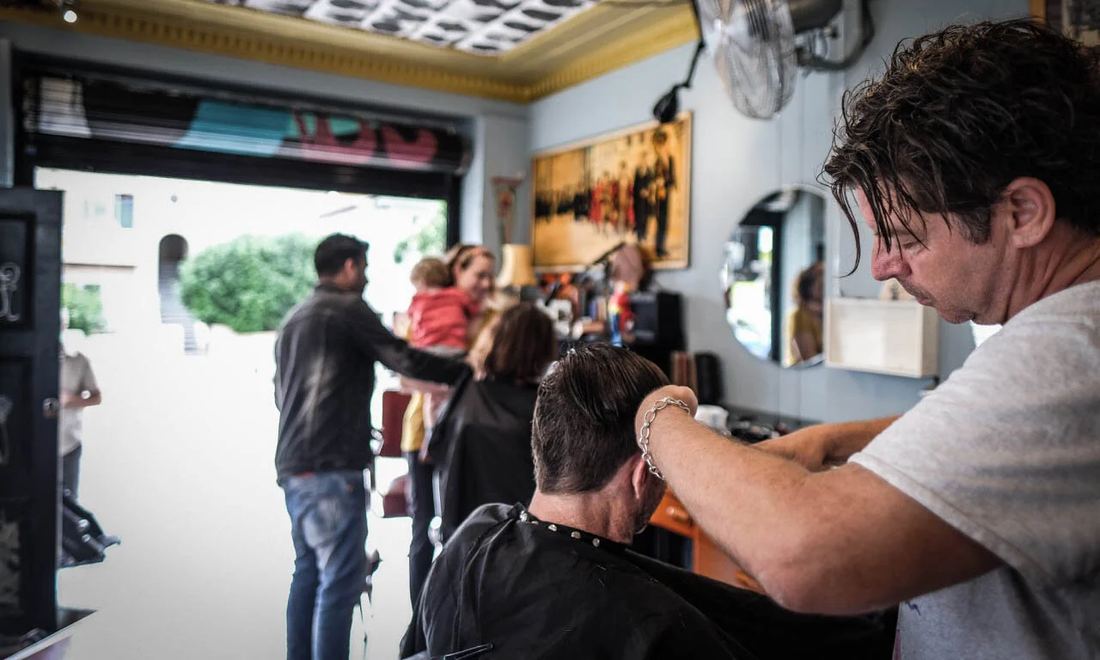 A Badlambs barber mid-cut while families wait by the open shopfront in Bondi Beach
